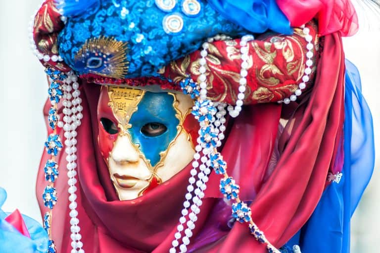 Close-up of a colorful Venetian carnival mask with ornate beads and rich fabrics.