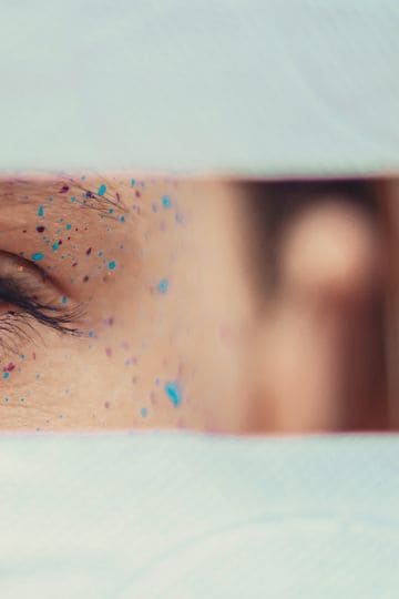 Selective focus crop calm female brown eye with multicolored paint spots on face skin looking at camera