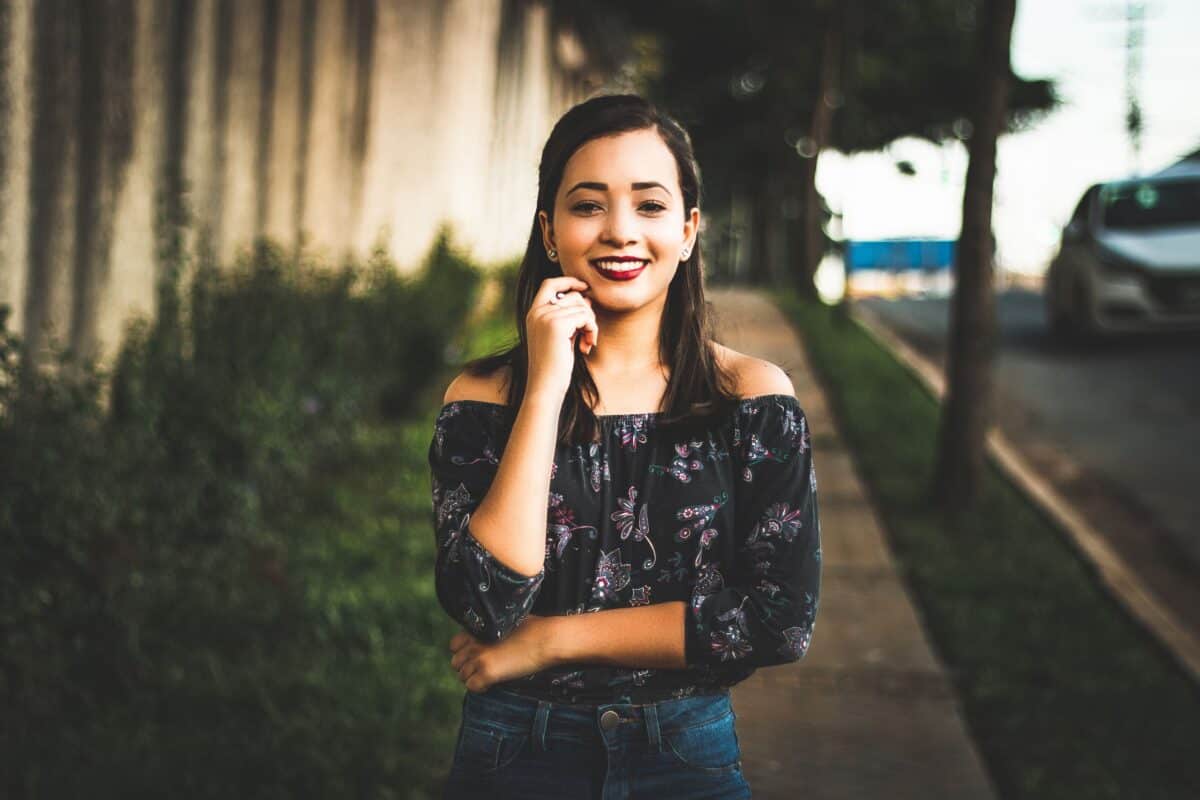 Smiling woman in casual wear posing confidently on a sunny city street.
